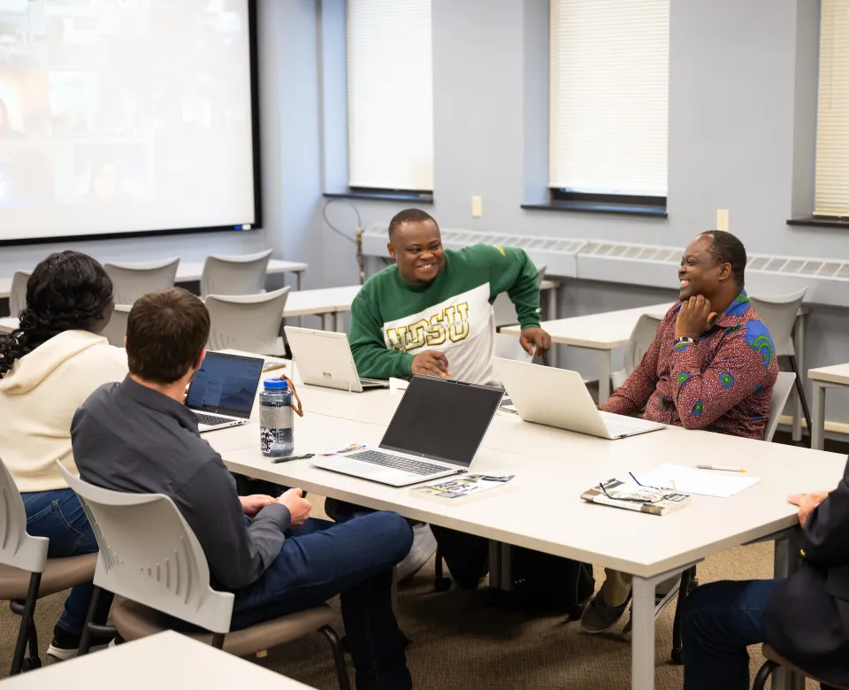 Students sitting around table with laptops open.