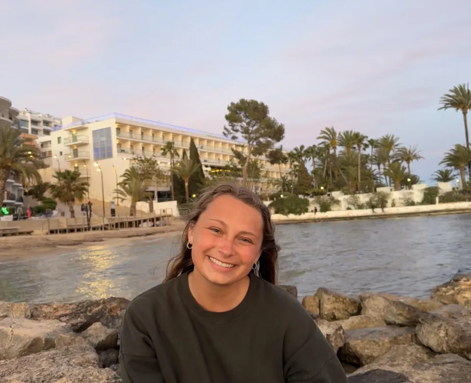 Student on top of rocks in front of a body of water and large building