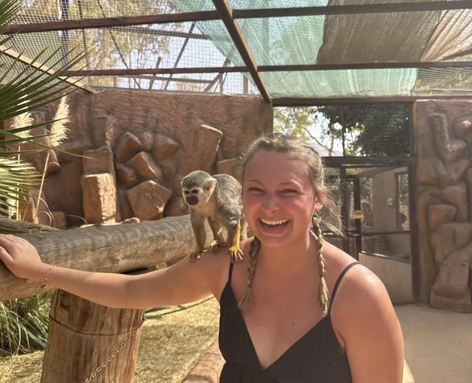 Student inside an animal exhibit with monkey on their shoulder