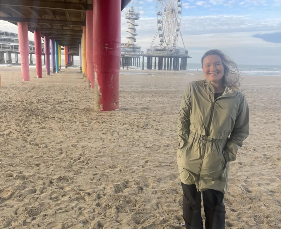 Student underneath bridge on beach in front of ferries wheel