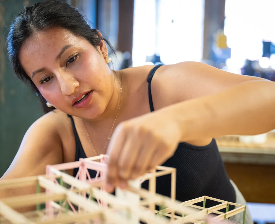 A student builds an architectural design using wooden sticks