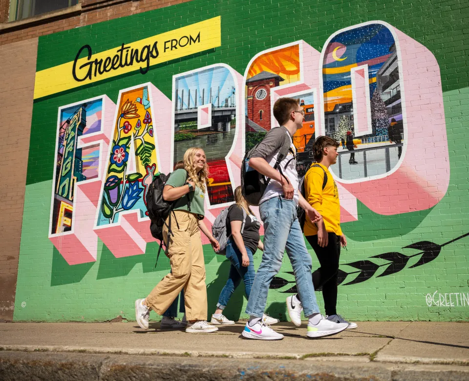 A group of NDSU students walk by a Greetings from Fargo mural