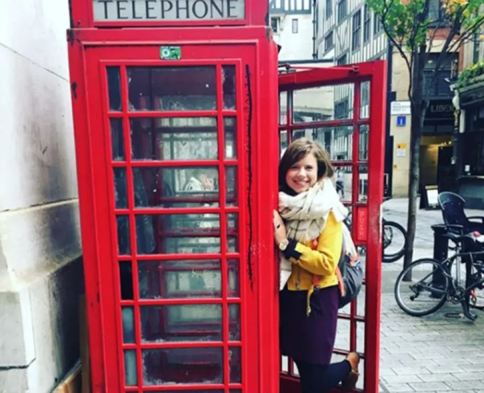 Student posing by a red telephone booth while smiling at camera.