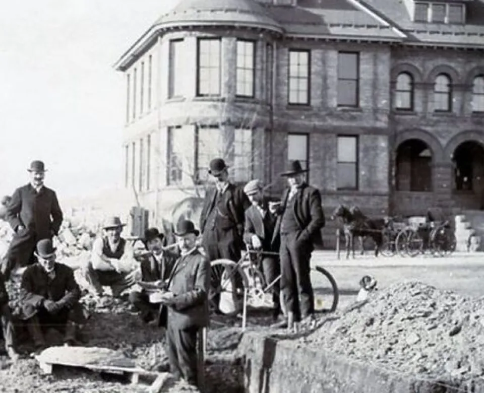 Black and white photo of men standing in front of historic building located on the NDSU campus.