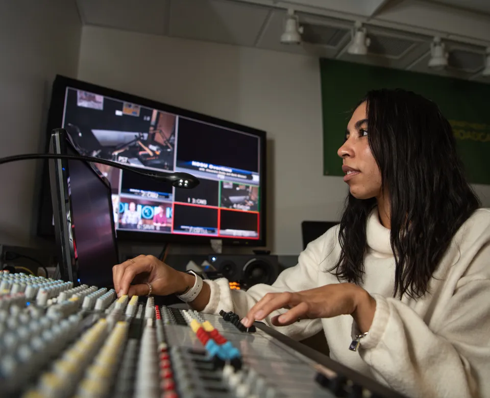Student working in a studio with tv monitors, computers and other equipment.