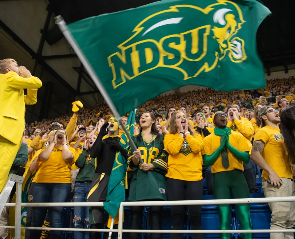 Students in the crowd cheering with Cheerleader. One student is waving the NDSU flag.