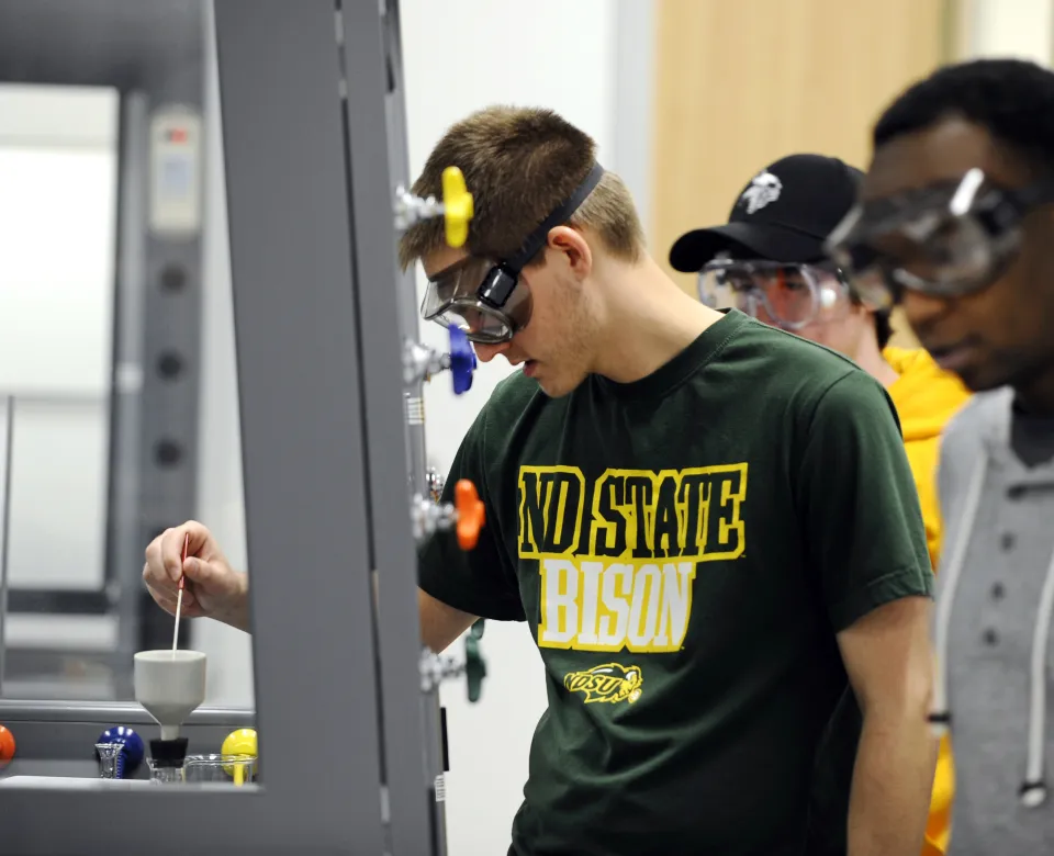 Student working in lab wearing goggles and a green NDSU Bison t-shirt