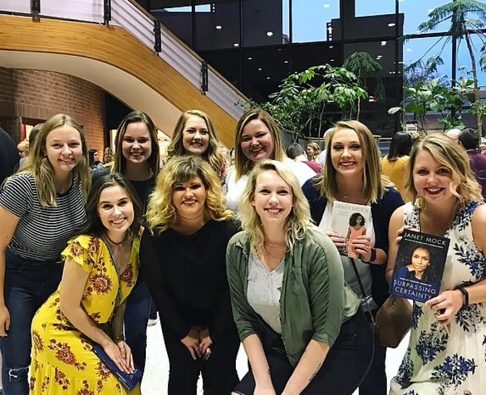 A group of women smiling confidently at the camera. Two of the women are holding books. 