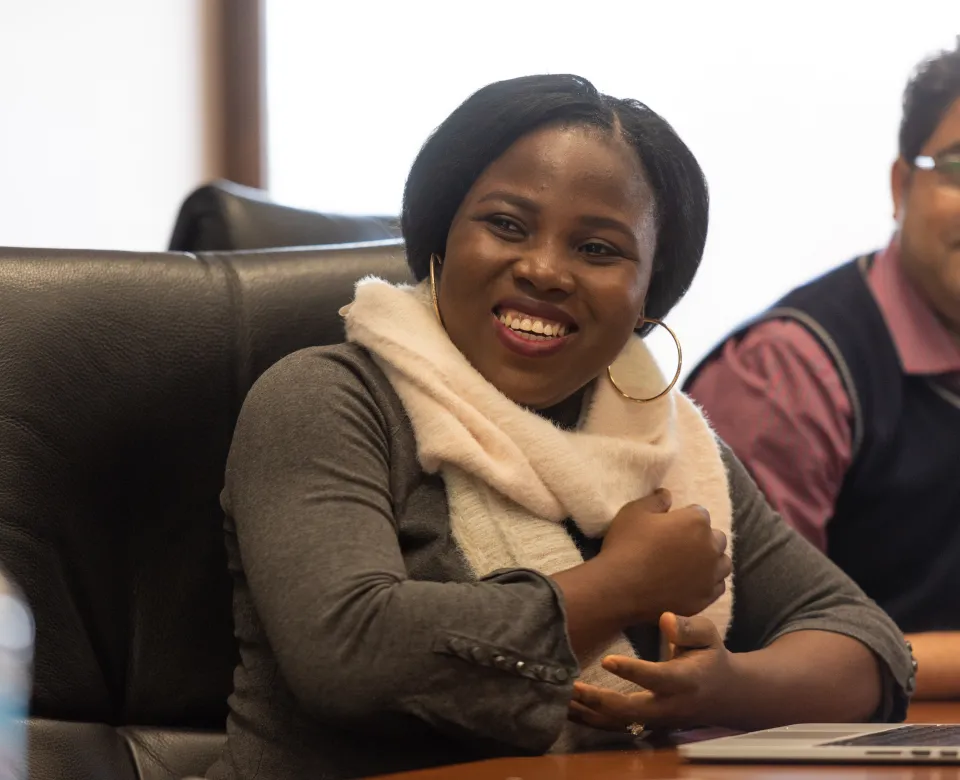 Student sitting at table with other students smiling and/or looking at the camera