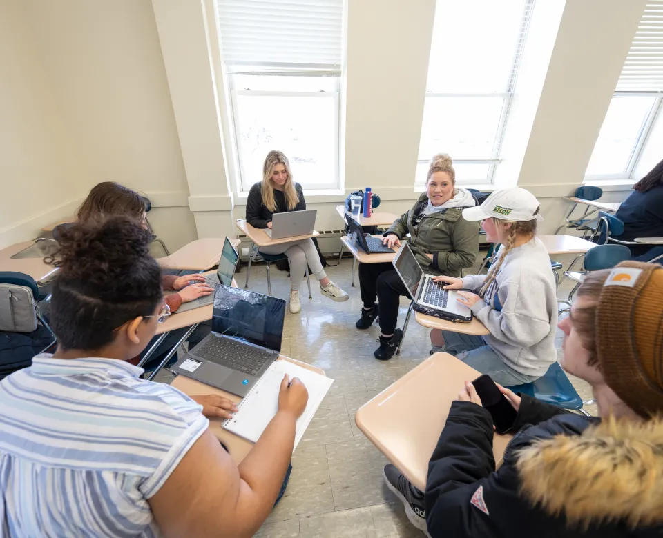 Students siting at desk arranged in a circle participating in a creative writing class