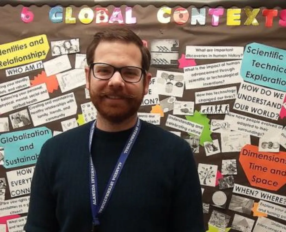 Mike Goulet standing in front of a bulletin board titled, 'Global Contexts'.