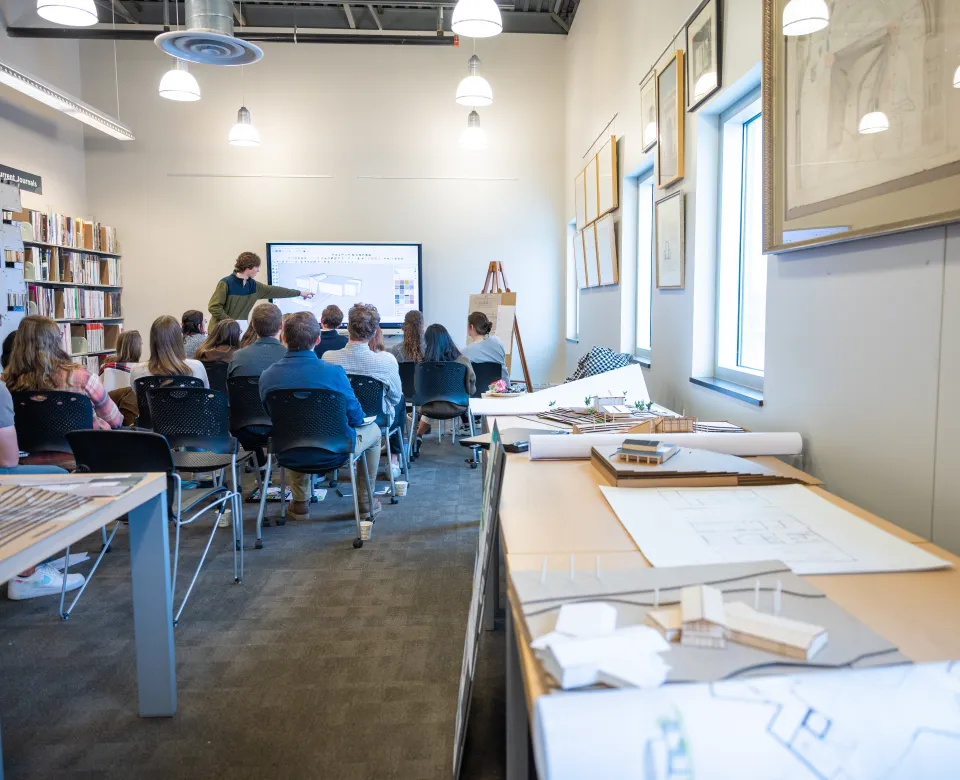 A group of students sitting in chairs while listening to someone present at front of room.