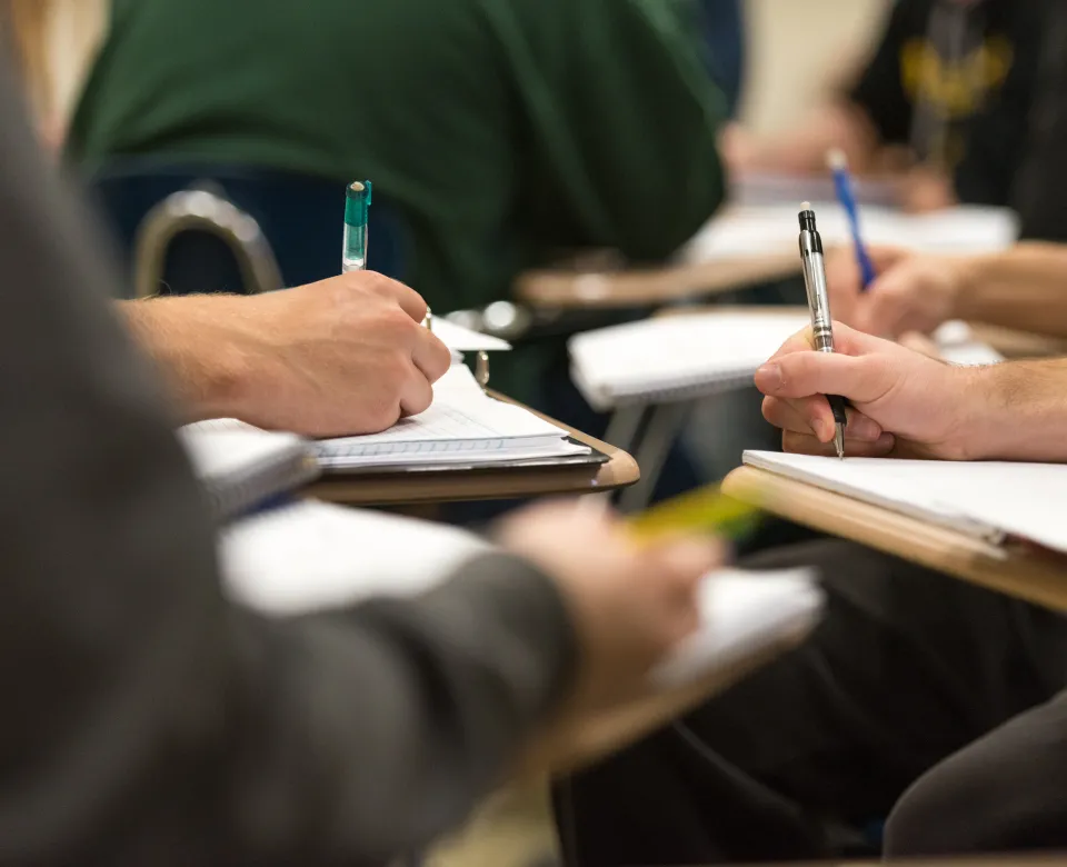 Students writing on notebooks  with pencil and pen while sitting at desks