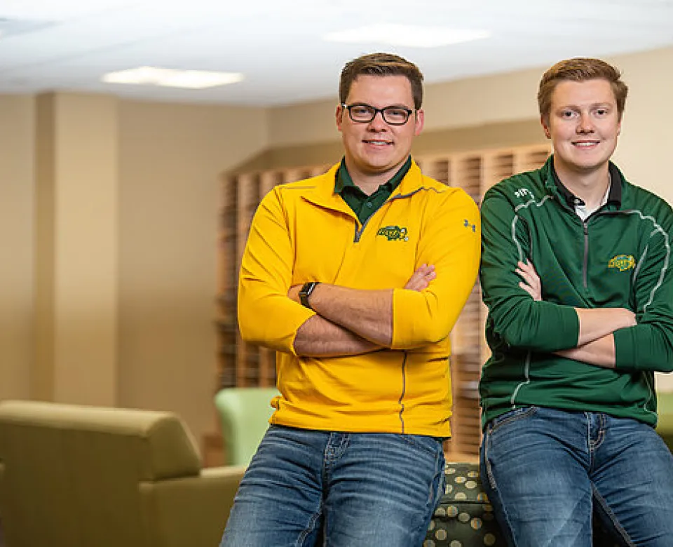 Students sitting on back of couch smiling at camera confidently with arms crossed.
