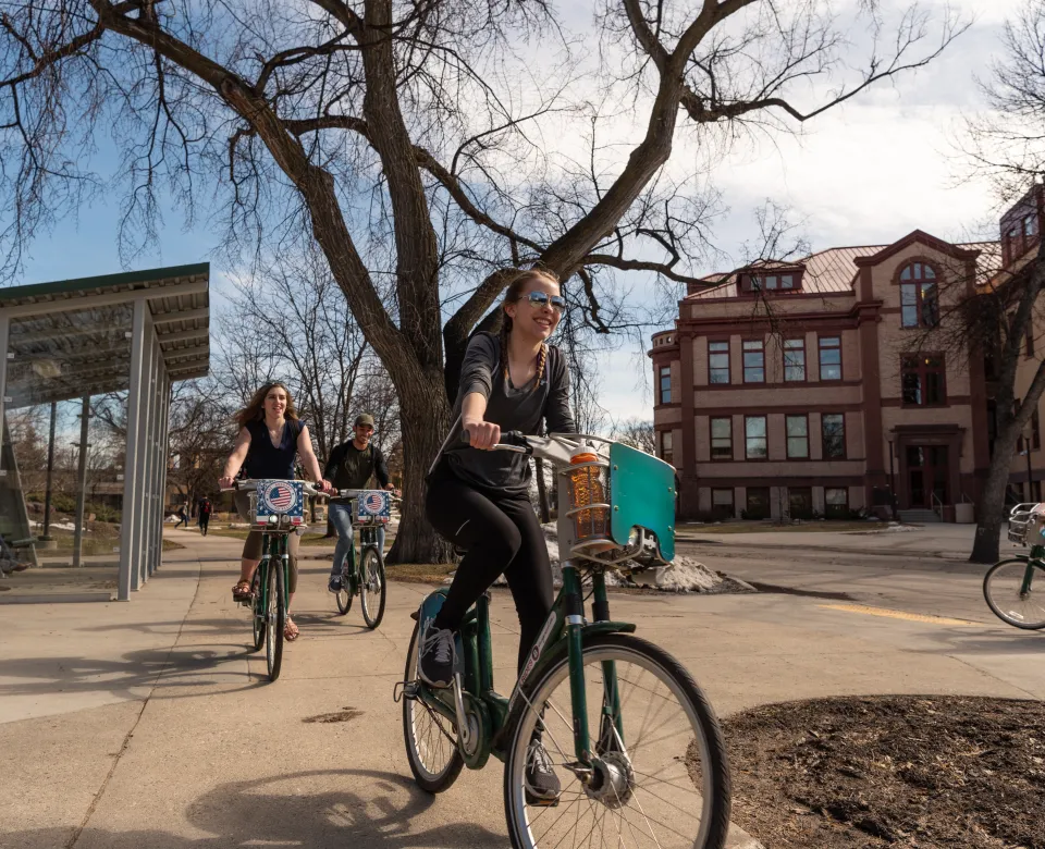 3 students riding bicycles on campus