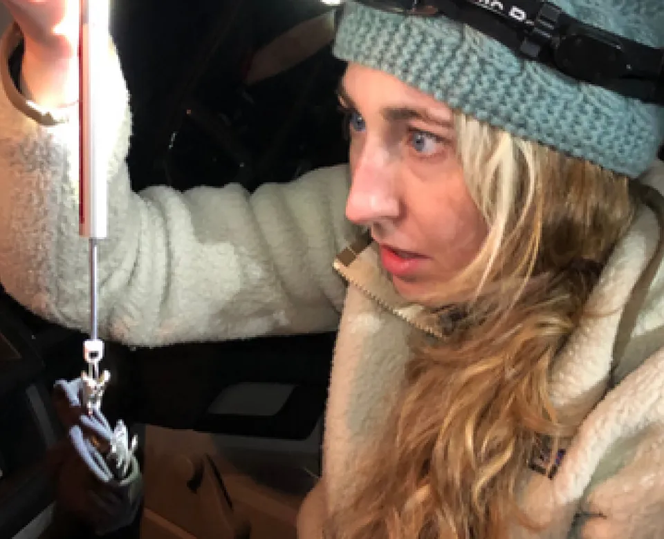 Woman wearing a headlamp weighing a frog. 