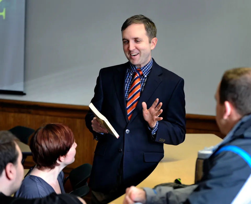 Dr. Beck holding a book and speaking to a group of students.