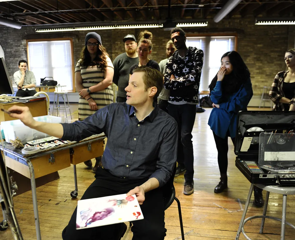Faculty teaching while painting in painting studio.