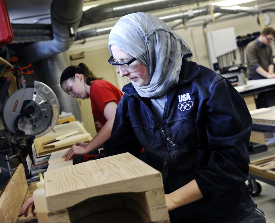 Student wearing protective eyeware while working with wood in woodship.
