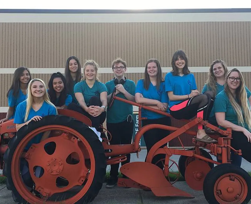 Group of students standing by a red vintage tractor. 