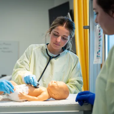 nursing students practicing infant patient care using a mannequin