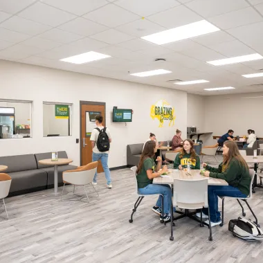 Outside shot of the Micro Market where three groups of students sit at tables talking and studying at Barry Hall