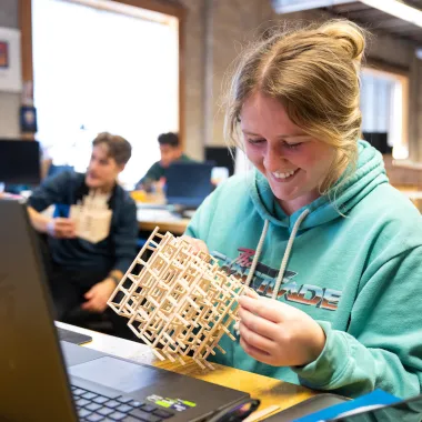 Student working with a wooden model while sitting in front of her computer.