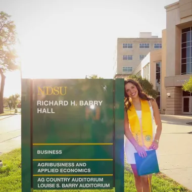 graduate standing by Barry Hall sign