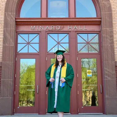 graduate in front of Minard Hall