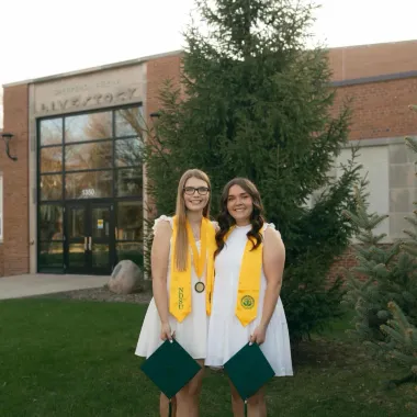 graduates standing in front of Sheppard Arena