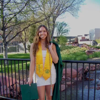 graduate in front of the babbling brook on campus