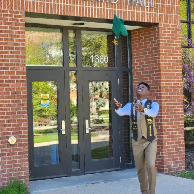 graduate throwing his cap into the air in front of Loftsgard Hall