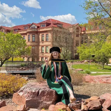 graduate in front of the babbling brook on campus