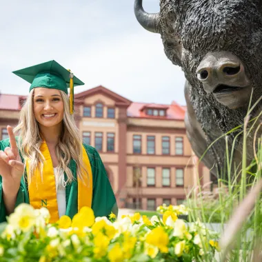 graduate giving bison horns next to bison statue