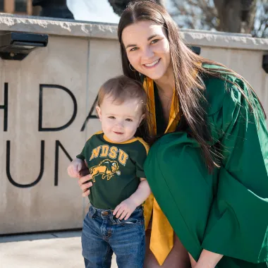 graduate posing with young bison fan in front of the bison statue