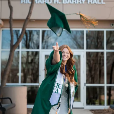 student throwing her graduation cap toward the camera in front of Barry Hall in downtown Fargo