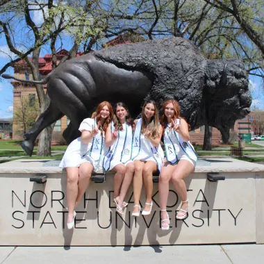 group of students sitting at the Bison Statue and giving bison horns