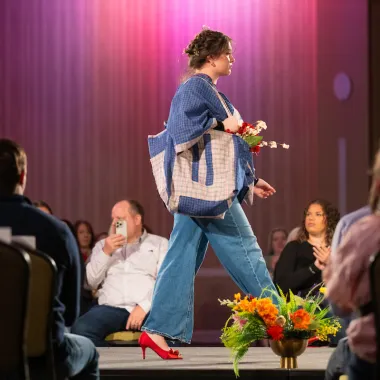 Model wearing jeans with red shoes while carring bag.