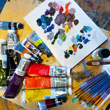 Art supplies layed out on table top including acrylic paint, paint brushes, canvas.