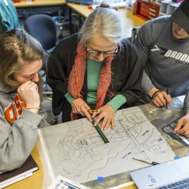 Faculty working with rendering on paper while instructing two students. 