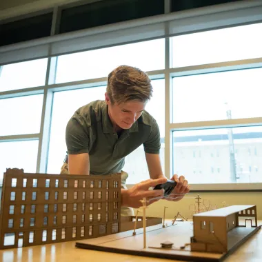 Architecture student working on a model-sized structure sitting on top of table.