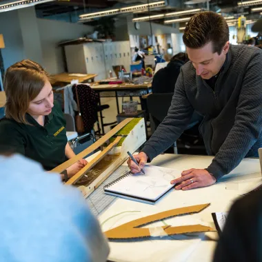 Students watching professor as he instructs using pen and paper in design studio.