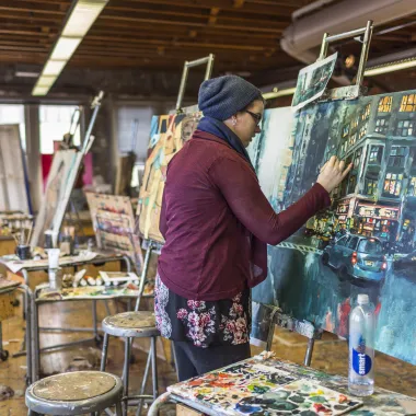 Visual arts student painting on project displayed on easel. 