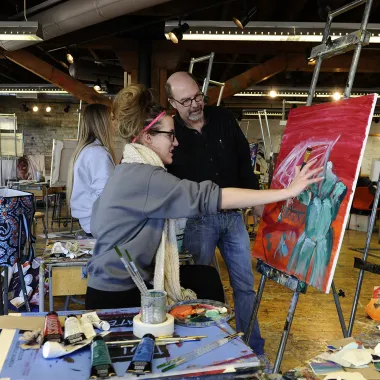 Faculty works with student in painting studio.