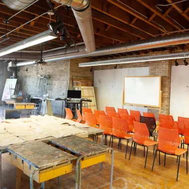 3 rows of chairs sitting between tables at back and white board at front of room.
