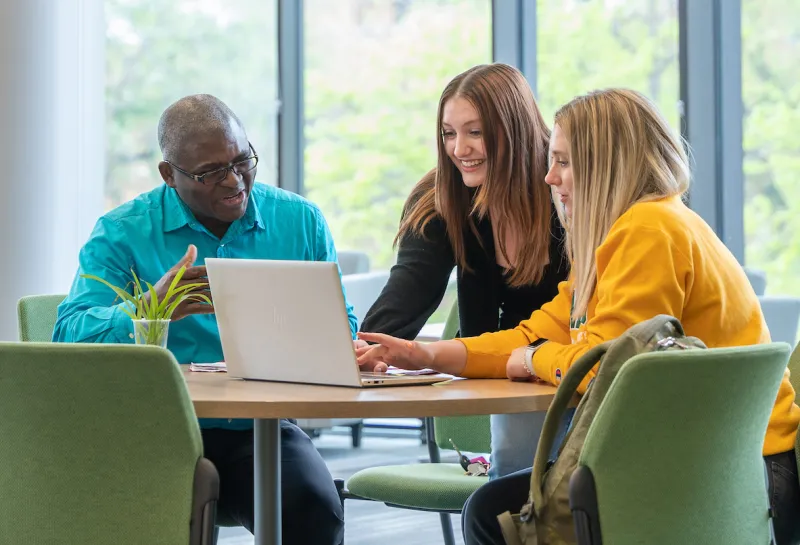 Graduate students are huddled around a laptop at a table.