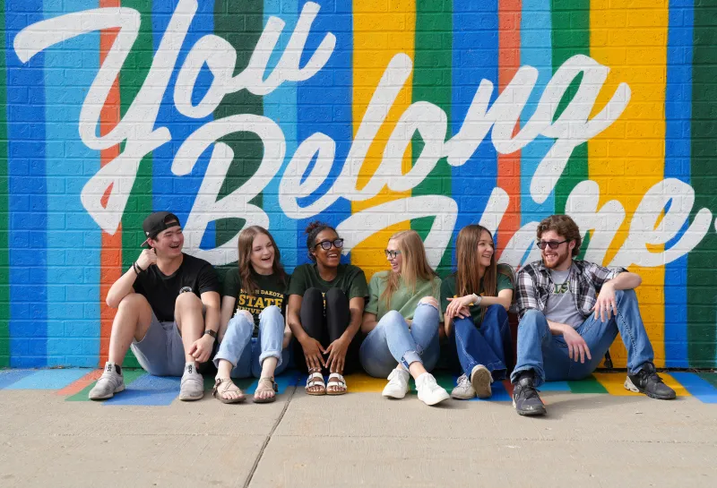 students sitting in front of You Belong Here mural