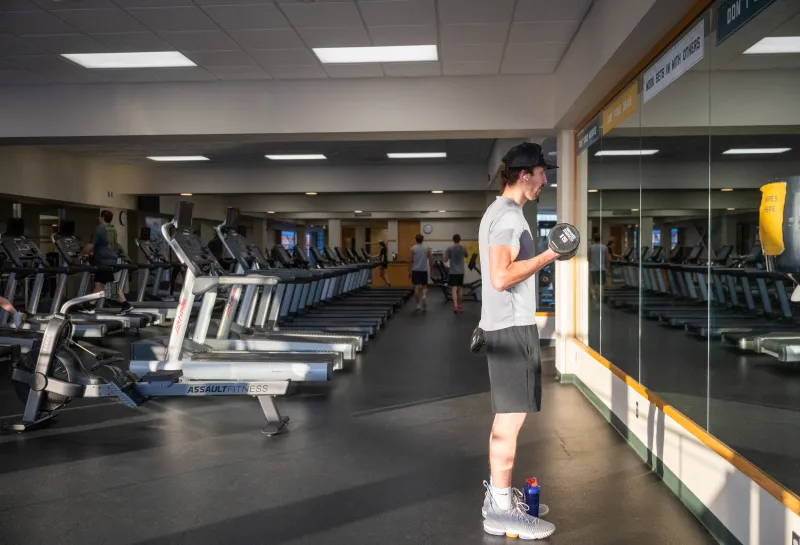 Student lifting weights in the Wellness Center by treadmills