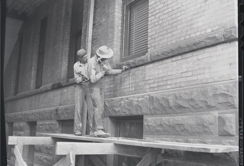 archive photo of 2 men working on the exterior of Old Main