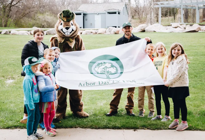 A group of people and a flickertail mascot hold up a flag smiling